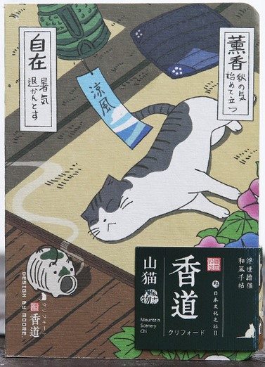 cover of a small notebook. it has a stylized drawing of a cat lying on a mat with its eyes closed